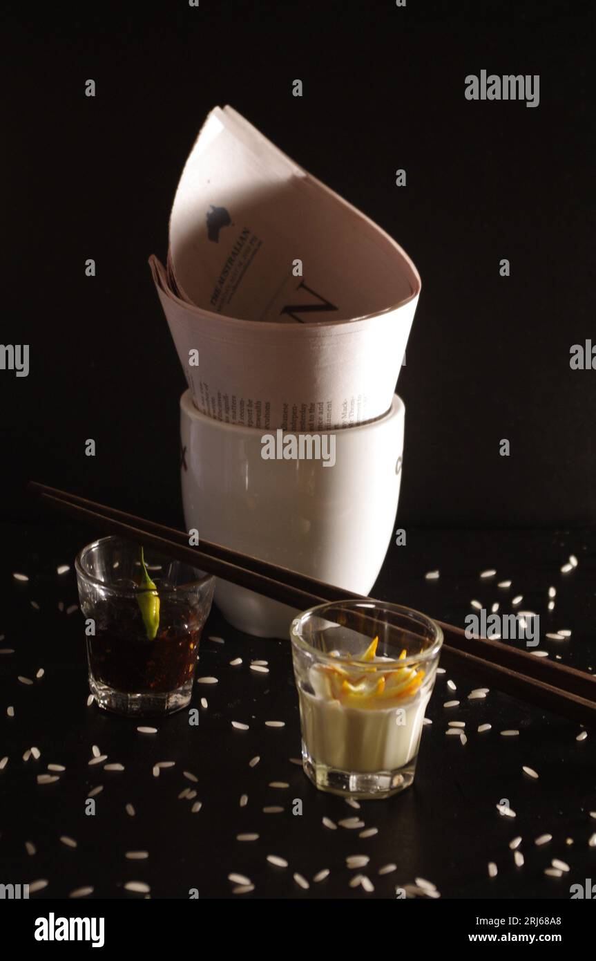 A white porcelain bowl and various sauces accompanied by chopsticks on a black background Stock Photo
