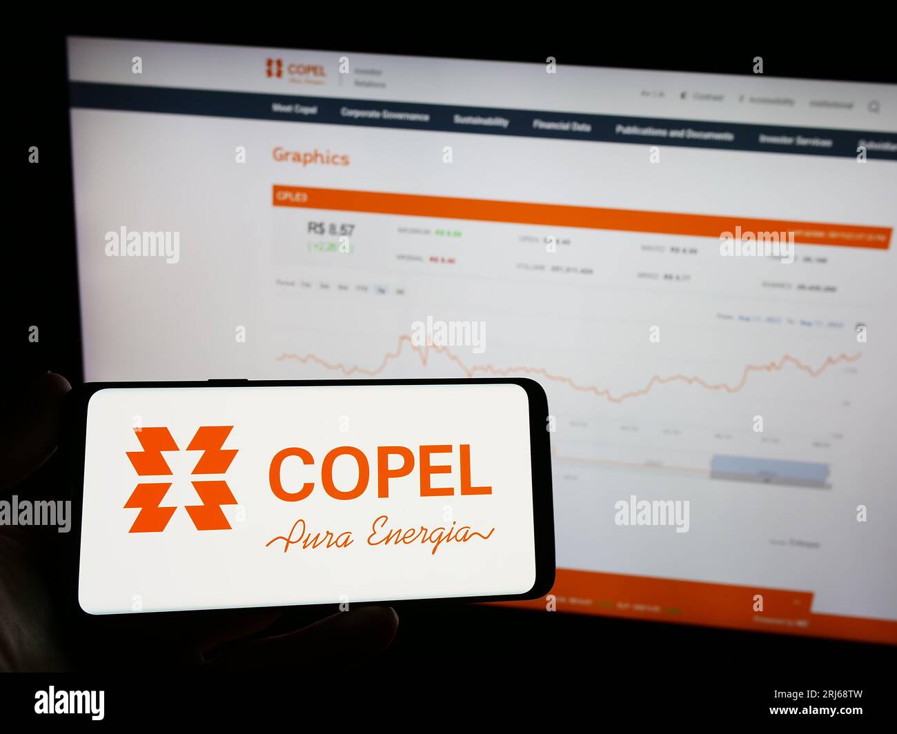 Person holding mobile phone with logo of company Companhia Paranaense de Energia (Copel) on screen in front of web page. Focus on phone display. Stock Photo