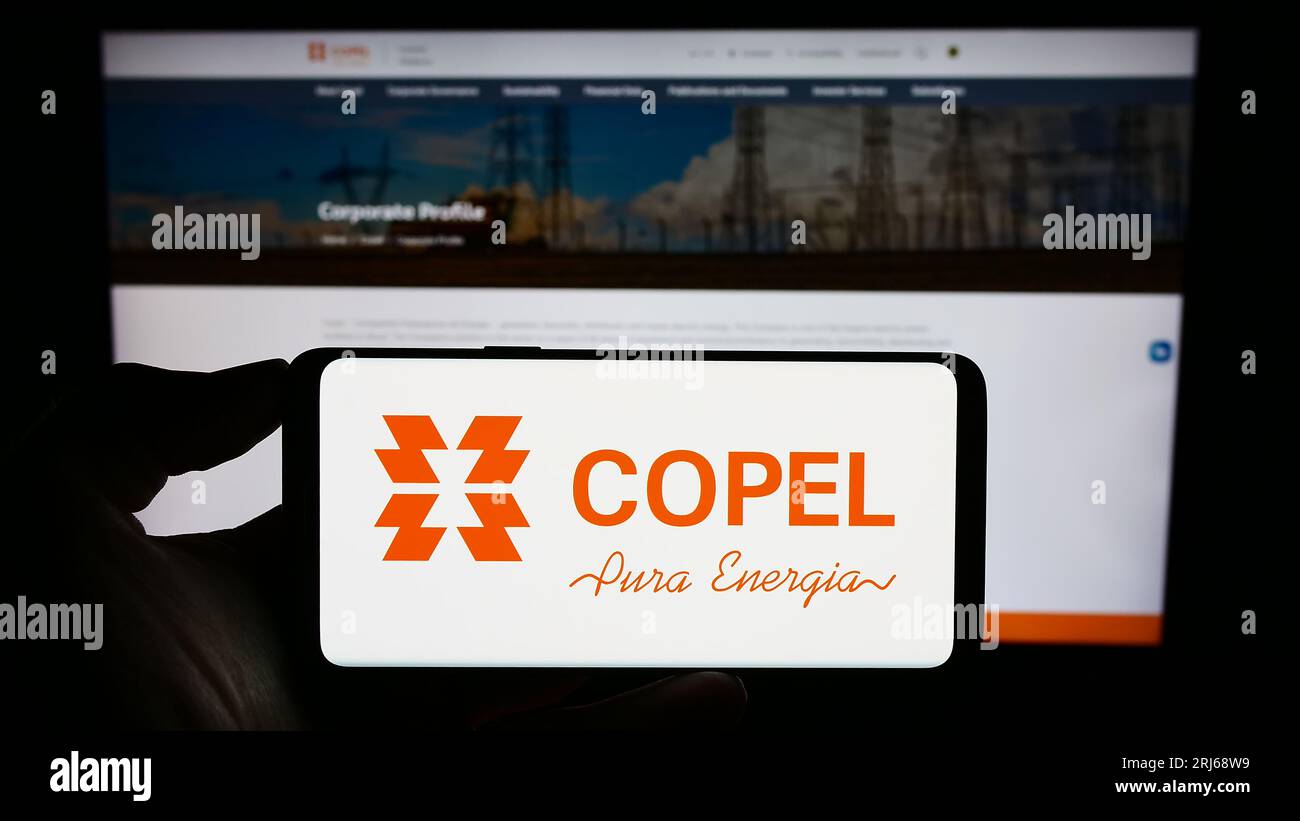 Person holding smartphone with logo of company Companhia Paranaense de Energia (Copel) on screen in front of website. Focus on phone display. Stock Photo