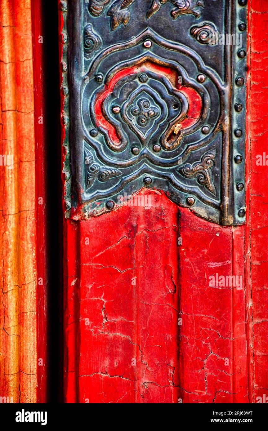 An orange door with peeling paint, featuring metal hardware fixtures