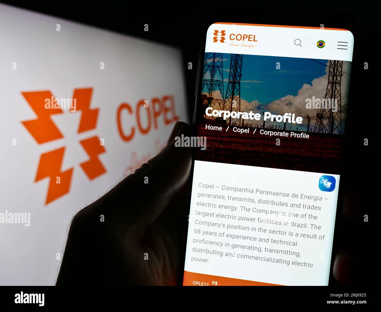 Person holding cellphone with webpage of company Companhia Paranaense de Energia (Copel) on screen with logo. Focus on center of phone display. Stock Photo