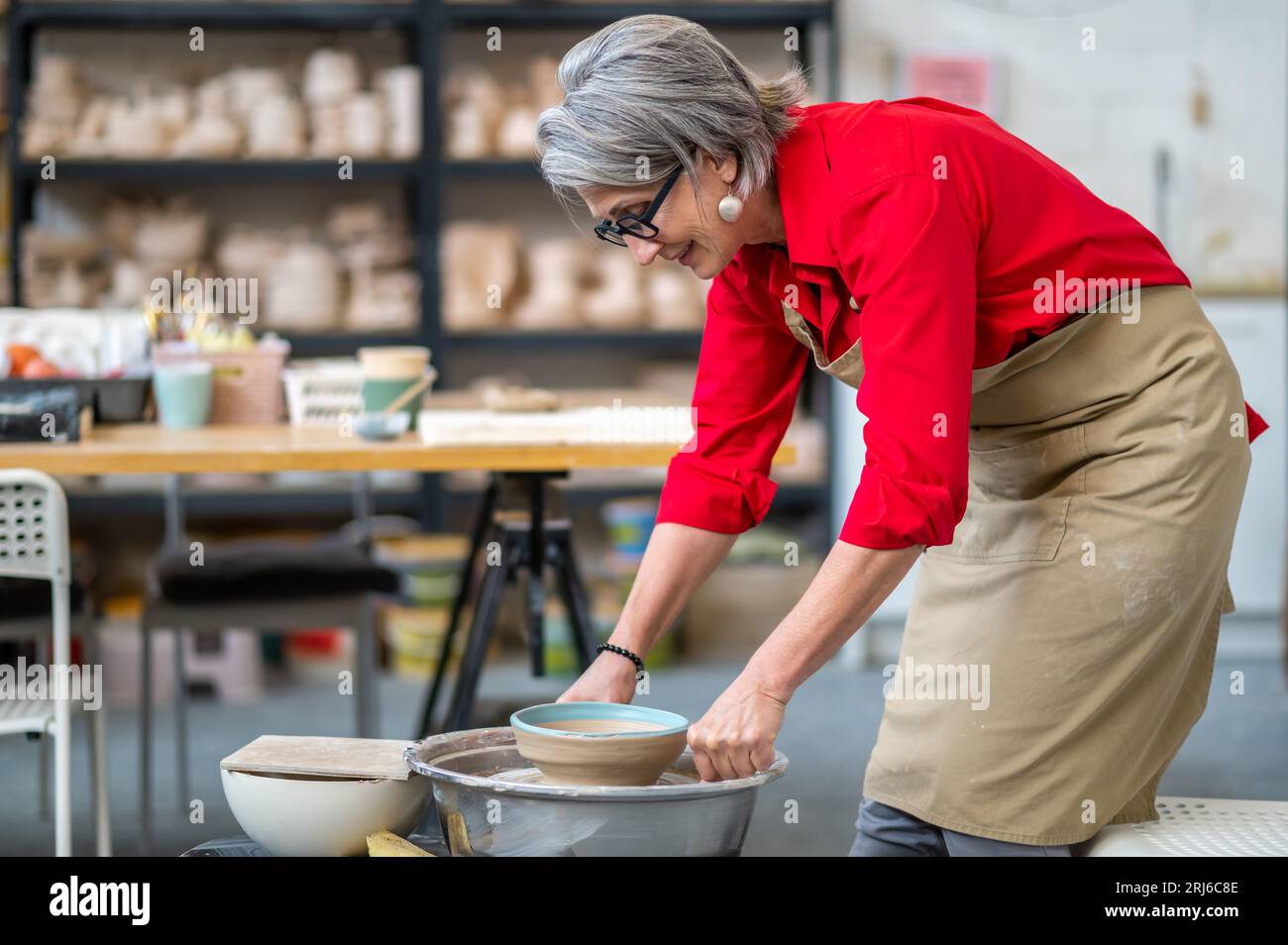 Woman potter taking finished plate from pottery wheel, making earthenware. Stock Photo
