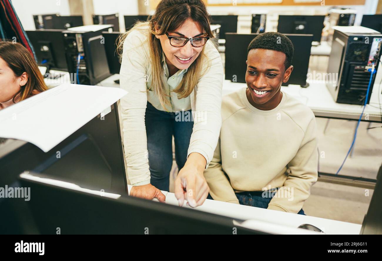 Young student learning how to use personal computer with his teacher at ...