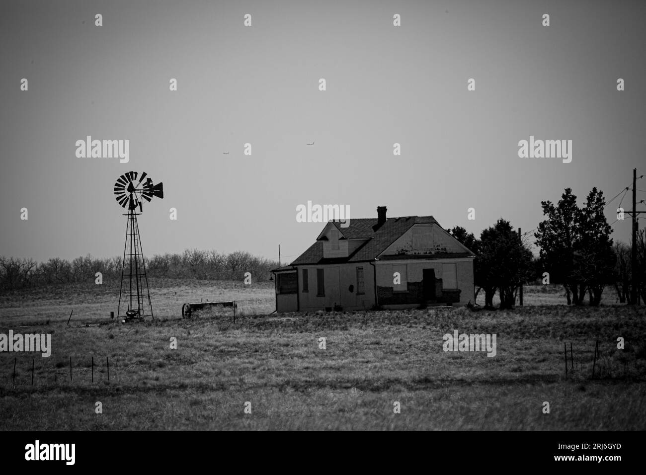 A black and white shot of a rustic, dilapidated farmhouse near a tranquil lake in Colorado Stock Photo