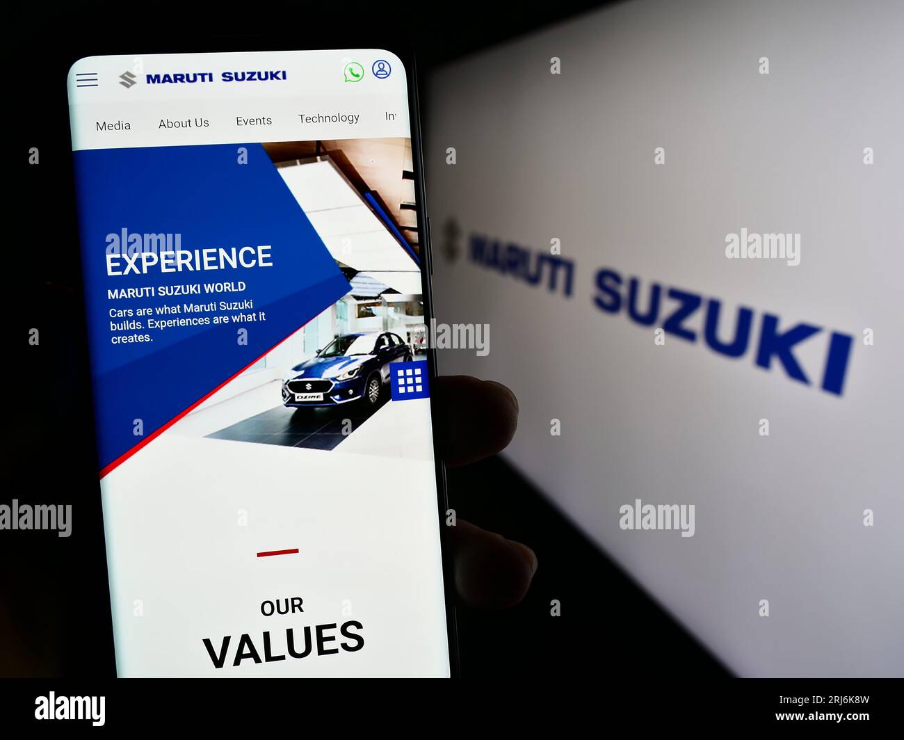 Person holding cellphone with webpage of Indian company Maruti Suzuki India Limited on screen in front of logo. Focus on center of phone display. Stock Photo
