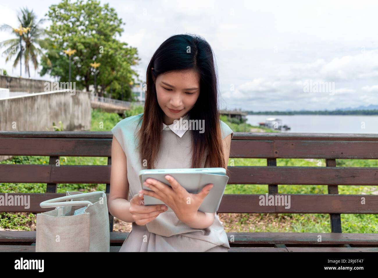 A young Southeast Asian woman using a tablet computer while sitting on ...