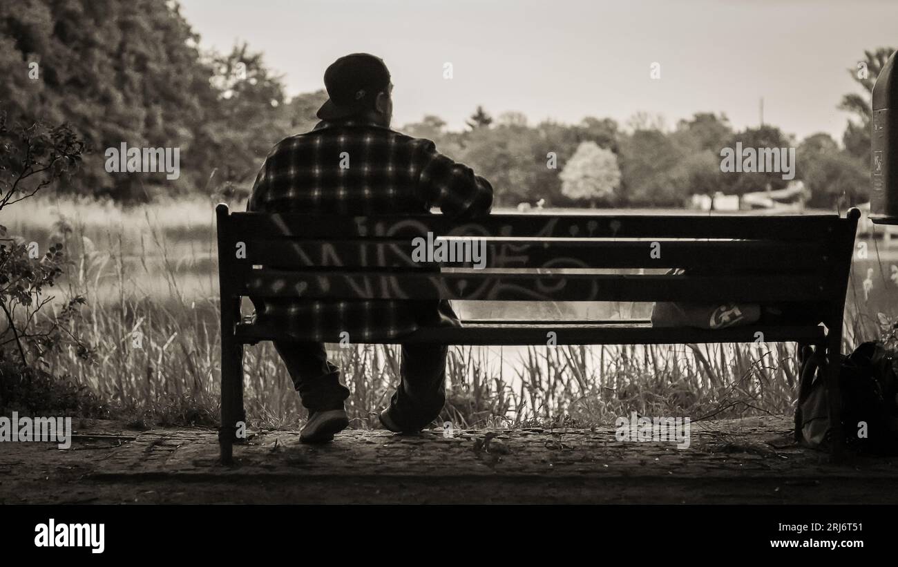 An adult male is seated on a bench with his arms crossed behind his ...