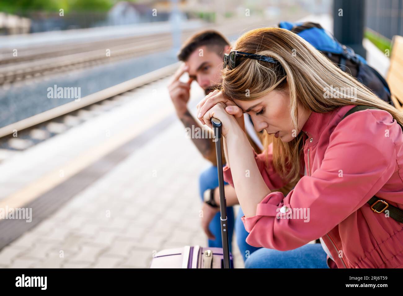 Tired couple sitting at railway station and waiting for arrival of their train. Stock Photo