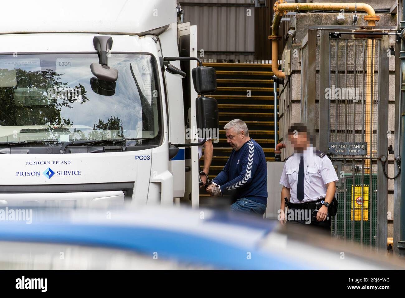 EDITORS NOTE IMAGE BLURRED BY PA PICTURE DESK Christopher Paul O'Kane (left) is led to a prison van after appearing at Ballymena Court, where he was charged with possessing documents or records likely to be useful to terrorists and possession of two mobile phones for use in terrorism. Picture date: Monday August 21, 2023. Stock Photo