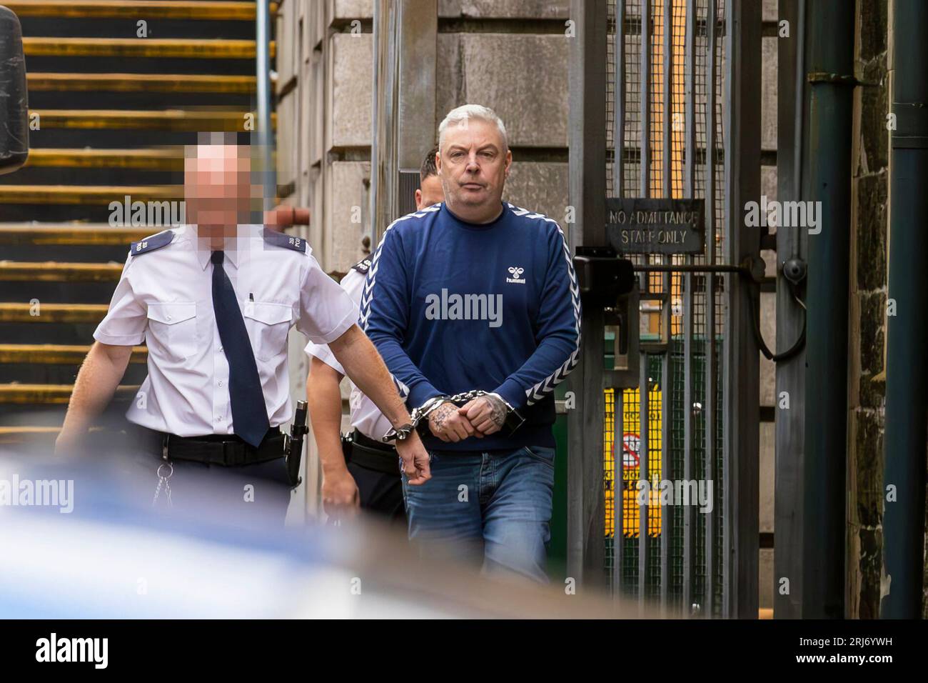 EDITORS NOTE IMAGE BLURRED BY PA PICTURE DESK Christopher Paul O'Kane (right) is led to a prison van after appearing at Ballymena Court, where he was charged with possessing documents or records likely to be useful to terrorists and possession of two mobile phones for use in terrorism. Picture date: Monday August 21, 2023. Stock Photo