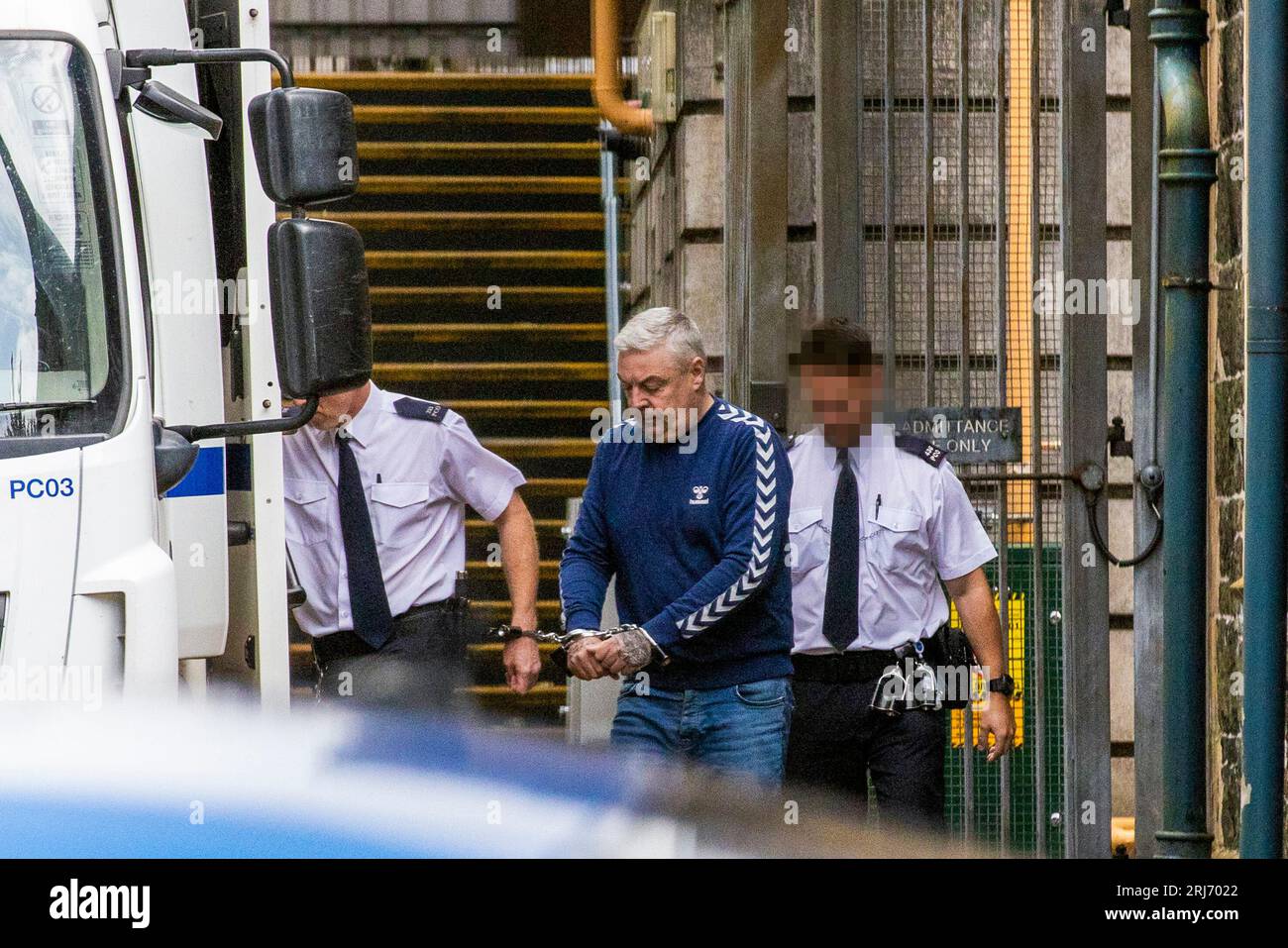EDITORS NOTE IMAGE BLURRED BY PA PICTURE DESK Christopher Paul O'Kane (centre) is led to a prison van after appearing at Ballymena Court, where he was charged with possessing documents or records likely to be useful to terrorists and possession of two mobile phones for use in terrorism. Picture date: Monday August 21, 2023. Stock Photo