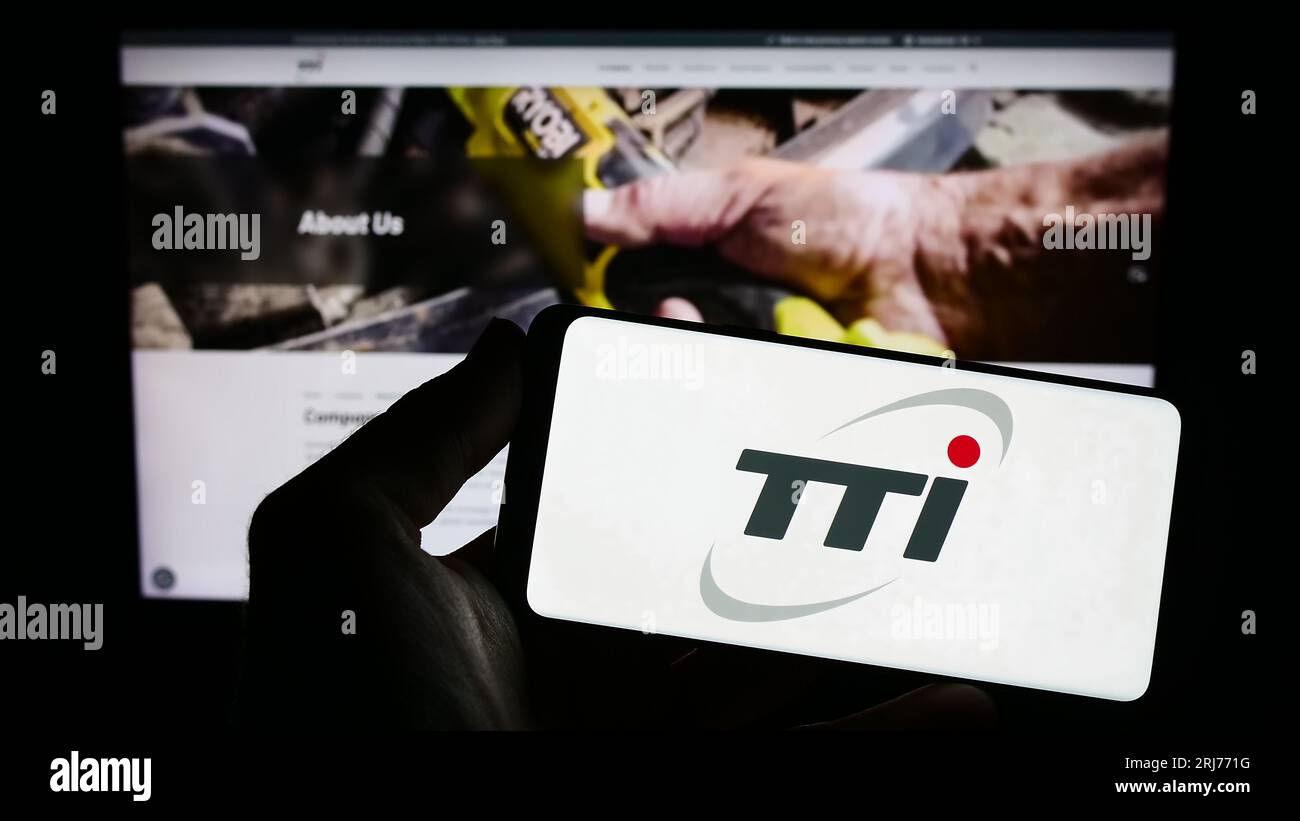Person holding smartphone with logo of Techtronic Industries Company Limited (TTI) on screen in front of website. Focus on phone display. Stock Photo