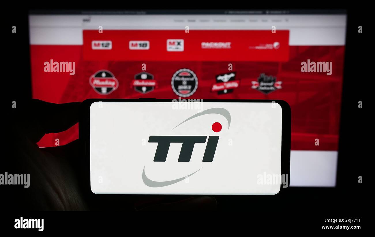Person holding cellphone with logo of Techtronic Industries Company Limited (TTI) on screen in front of business webpage. Focus on phone display. Stock Photo