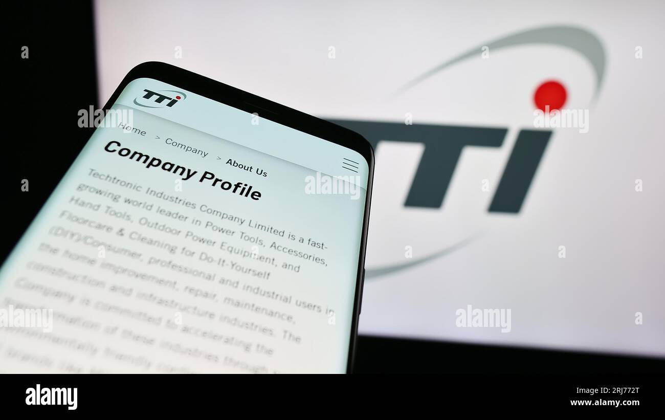 Mobile phone with website of Techtronic Industries Company Limited (TTI) on screen in front of business logo. Focus on top-left of phone display. Stock Photo