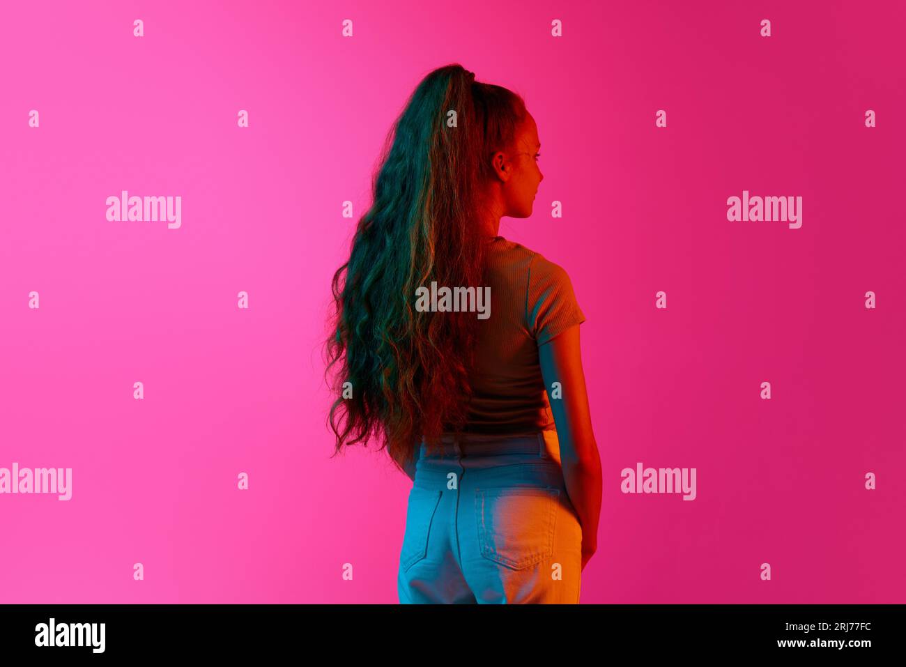 Back view of young girl with long curly hair in ponytail standing and ...