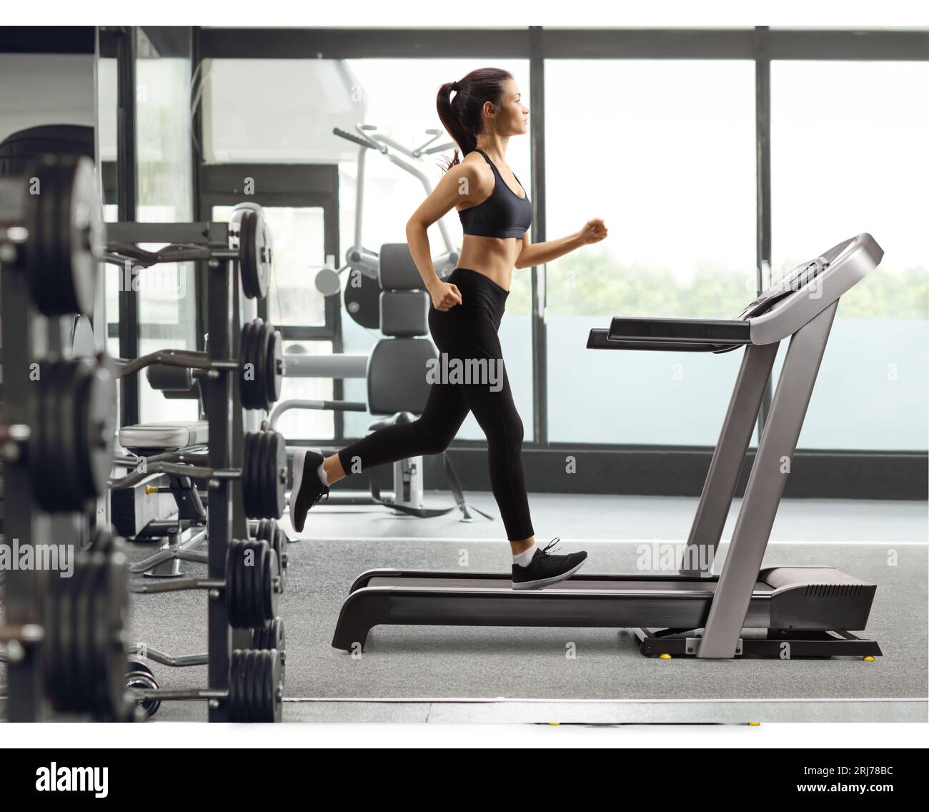 Full length profile shot of a young female in black leggings running on a treadmill at a gym Stock Photo