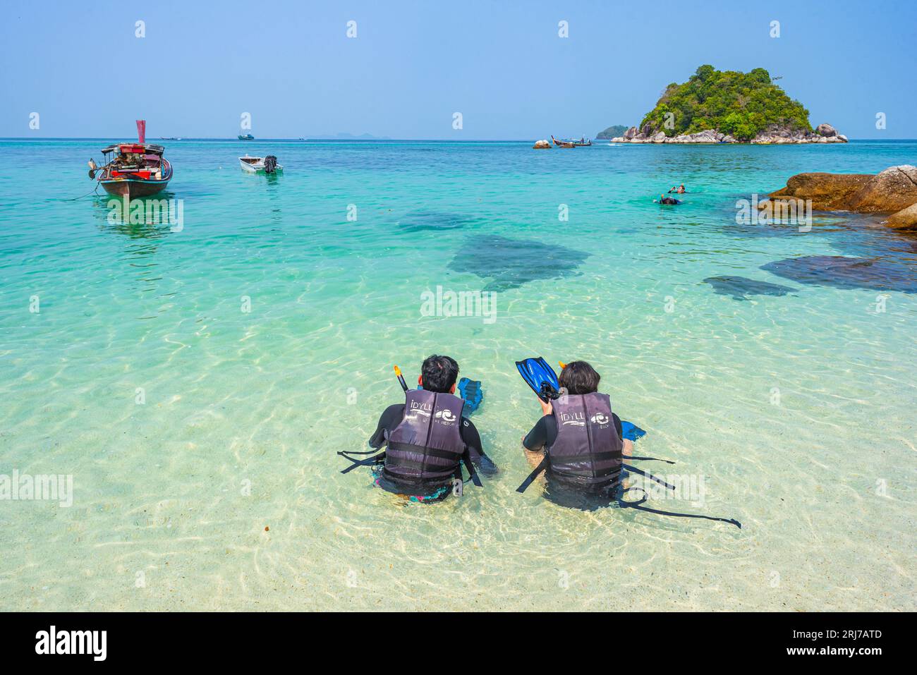 Ko Lipe, Thailand - April 11, 2023: two persons sit in the shallow sea water in life vests with snorkeling equipment at Sunrise Beach. Stock Photo