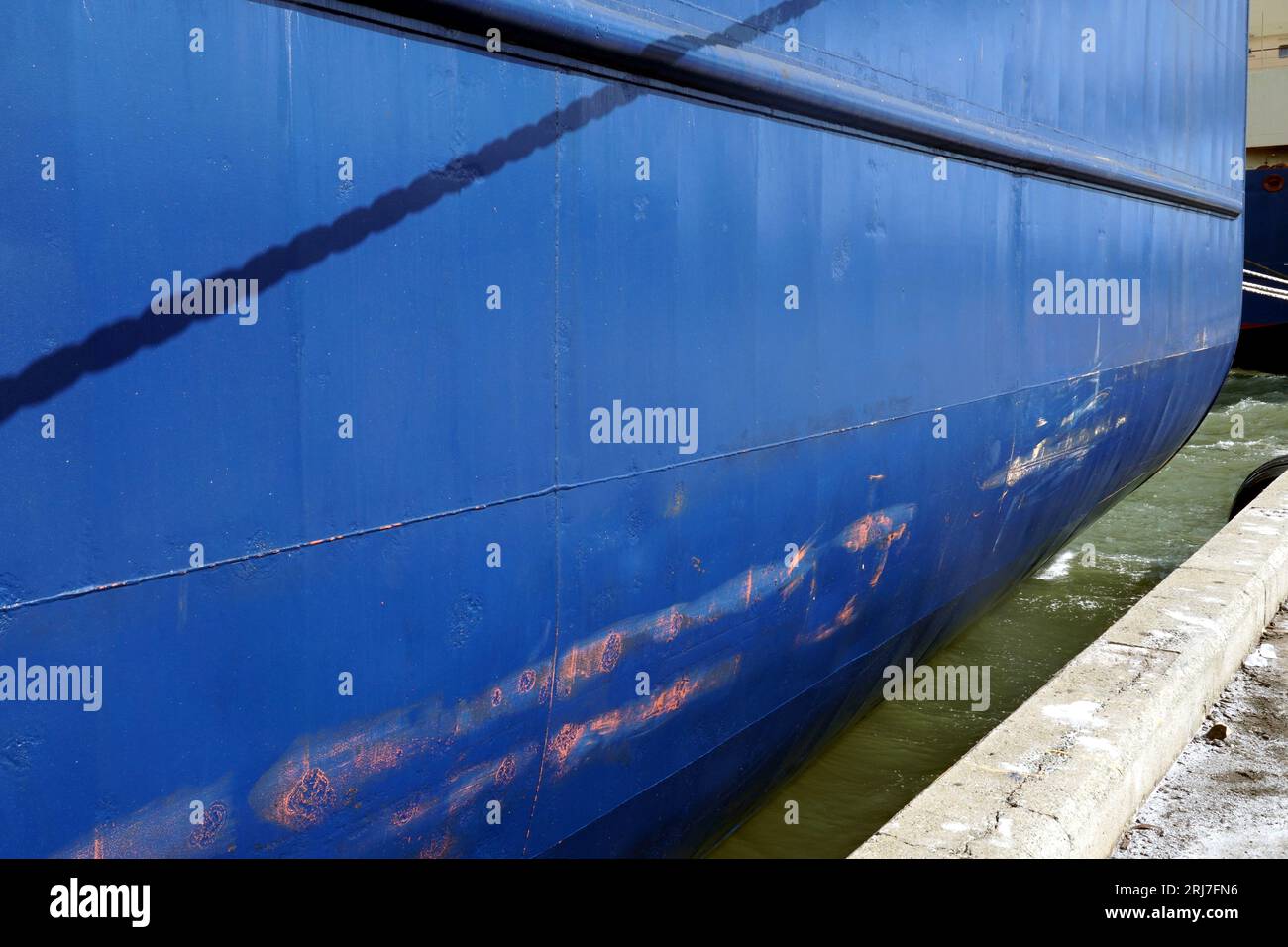 Vertical scratches and dents on the blue hull of container vessel moored in port. There are some rusty spots on the paint and copy space. Stock Photo