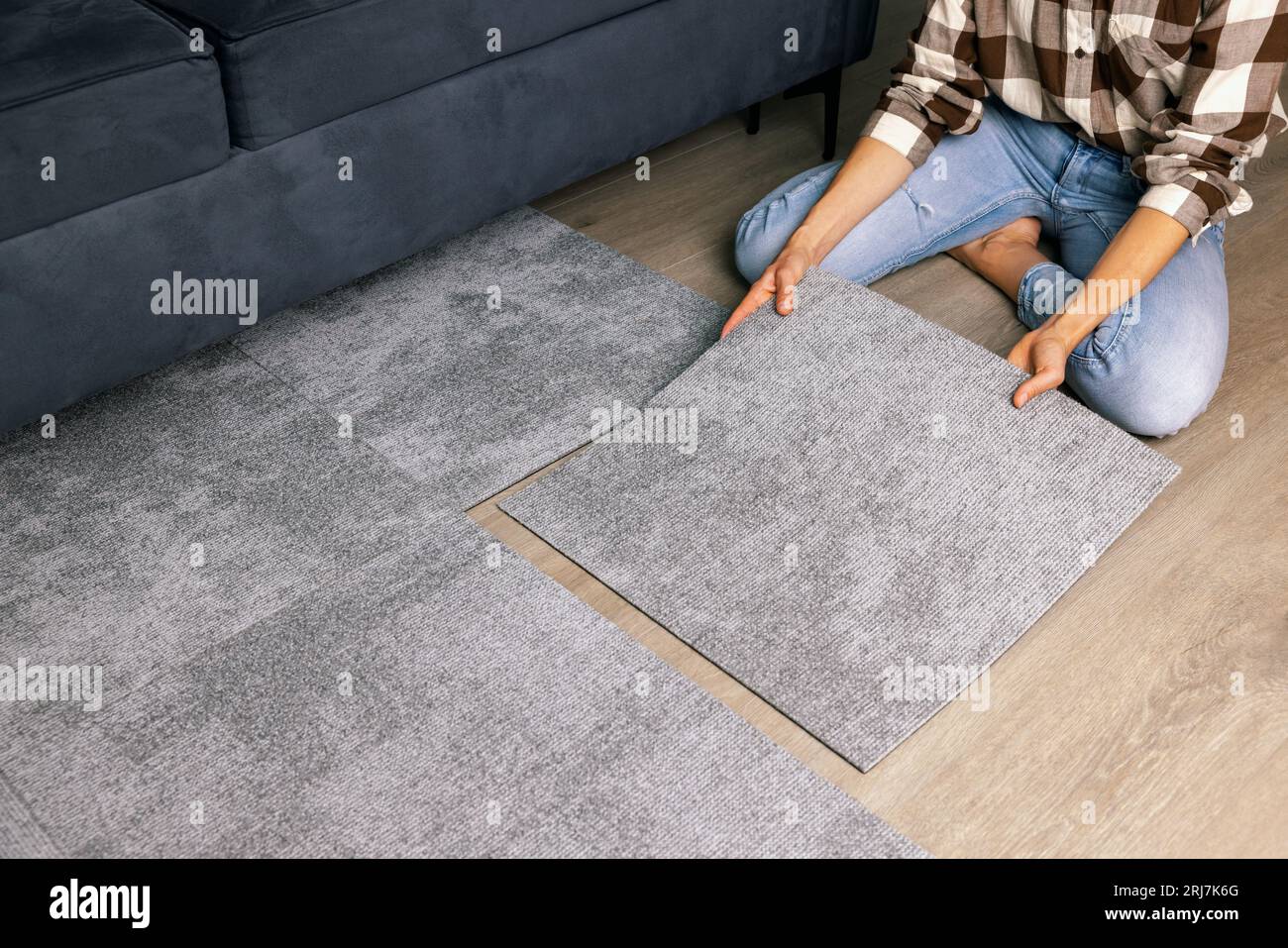 woman laying self adhesive carpet tiles on floor in living room at home Stock Photo