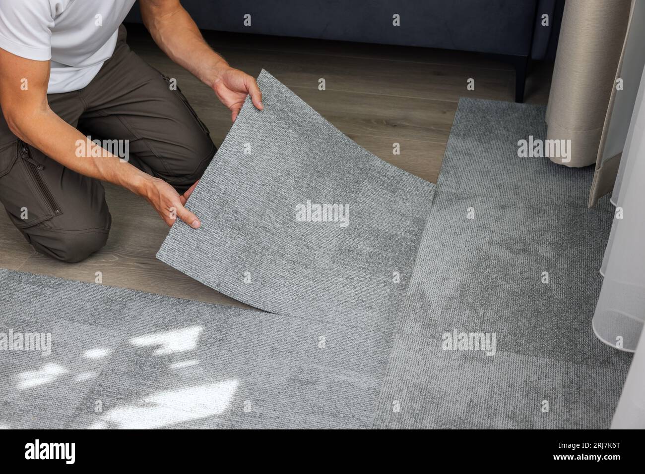 man installing self adhesive carpet tiles on floor in living room at home Stock Photo
