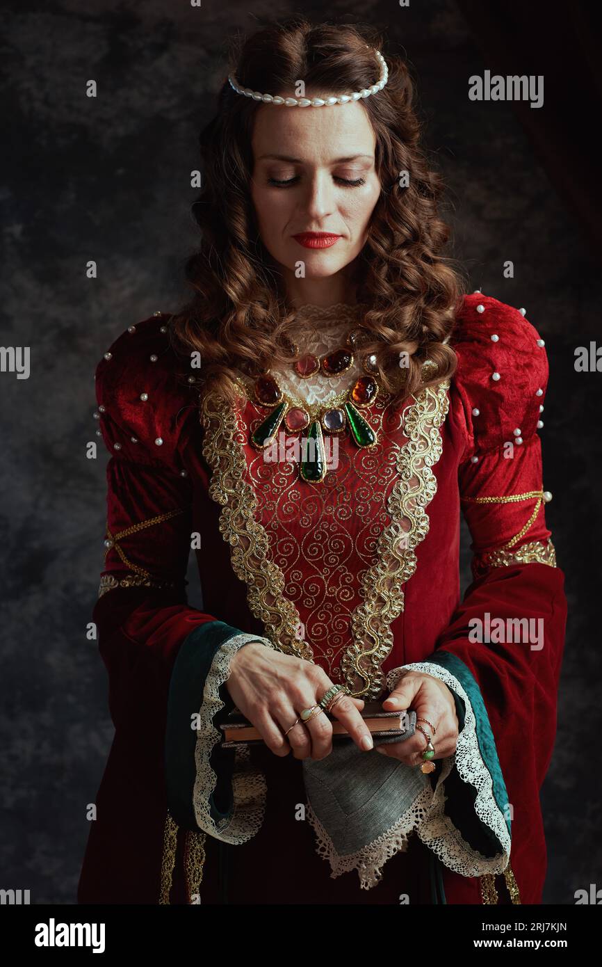 medieval queen in red dress with book and handkerchief on dark gray ...