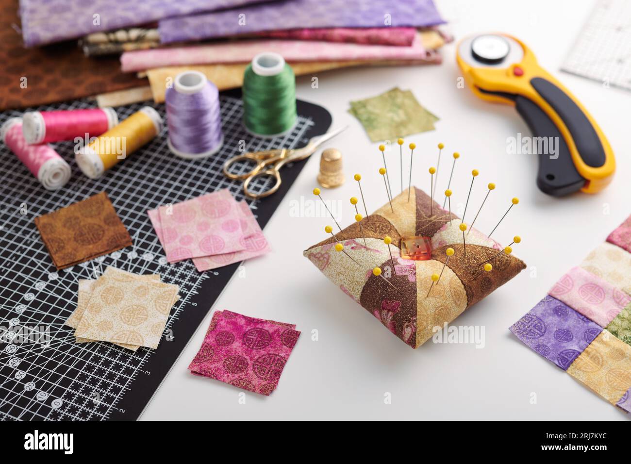 Pin cushion, stacks of square pieces of fabric, pile of patchwork fabrics, quilting and sewing