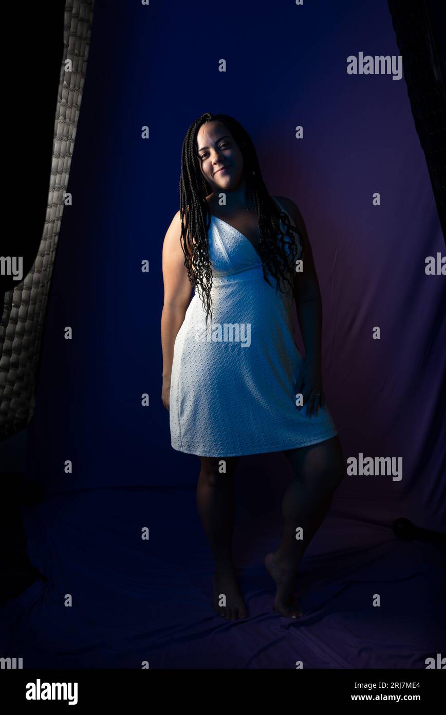 Studio portrait of pretty woman with braided hair in white dress posing for photo, standing. Isolated on dark blue colored background. Positive person Stock Photo
