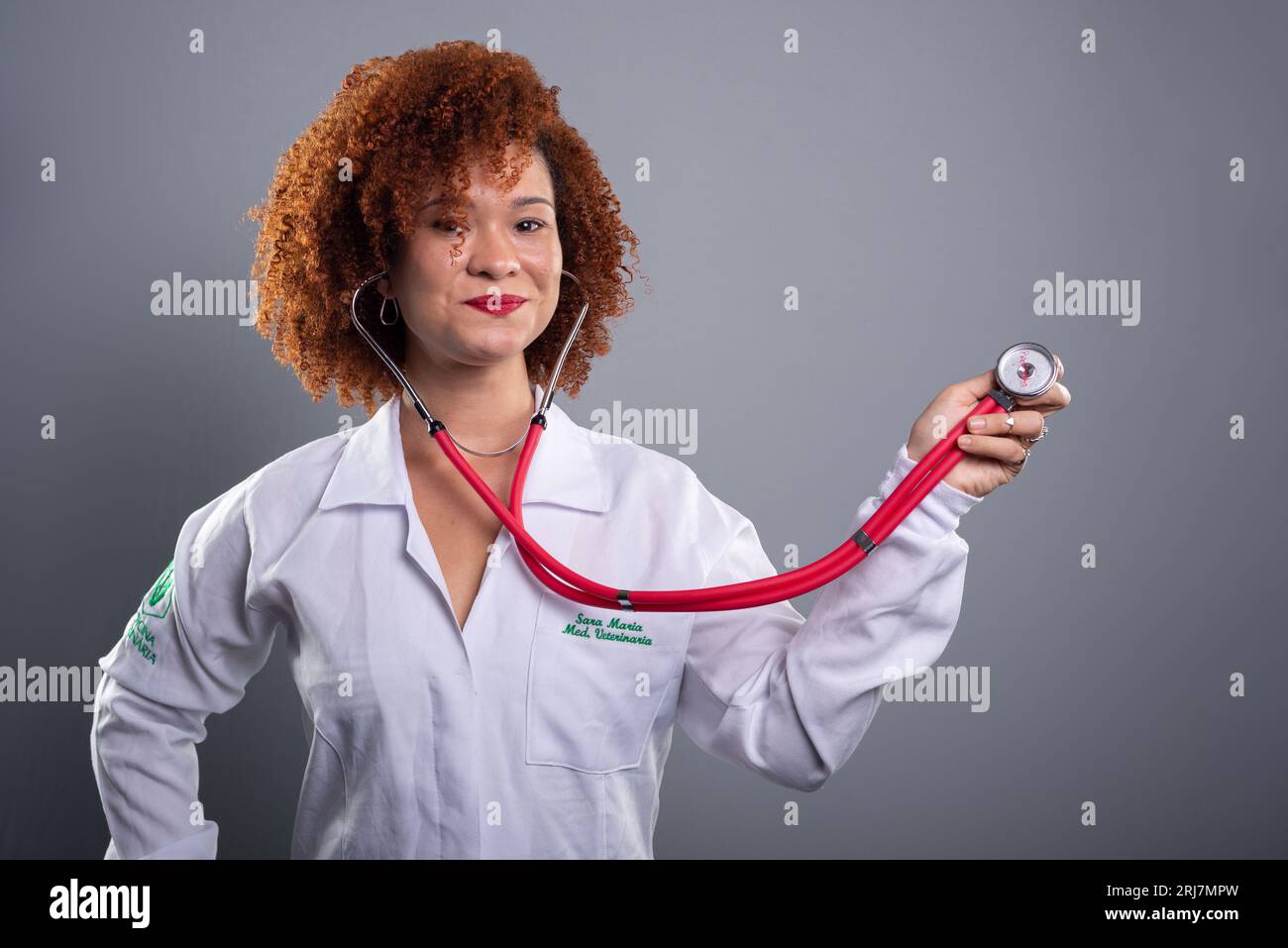Beautiful woman with red hair, veterinarian, holding a stethoscope in a white uniform. Animal care concept. Isolated on gray background. Stock Photo
