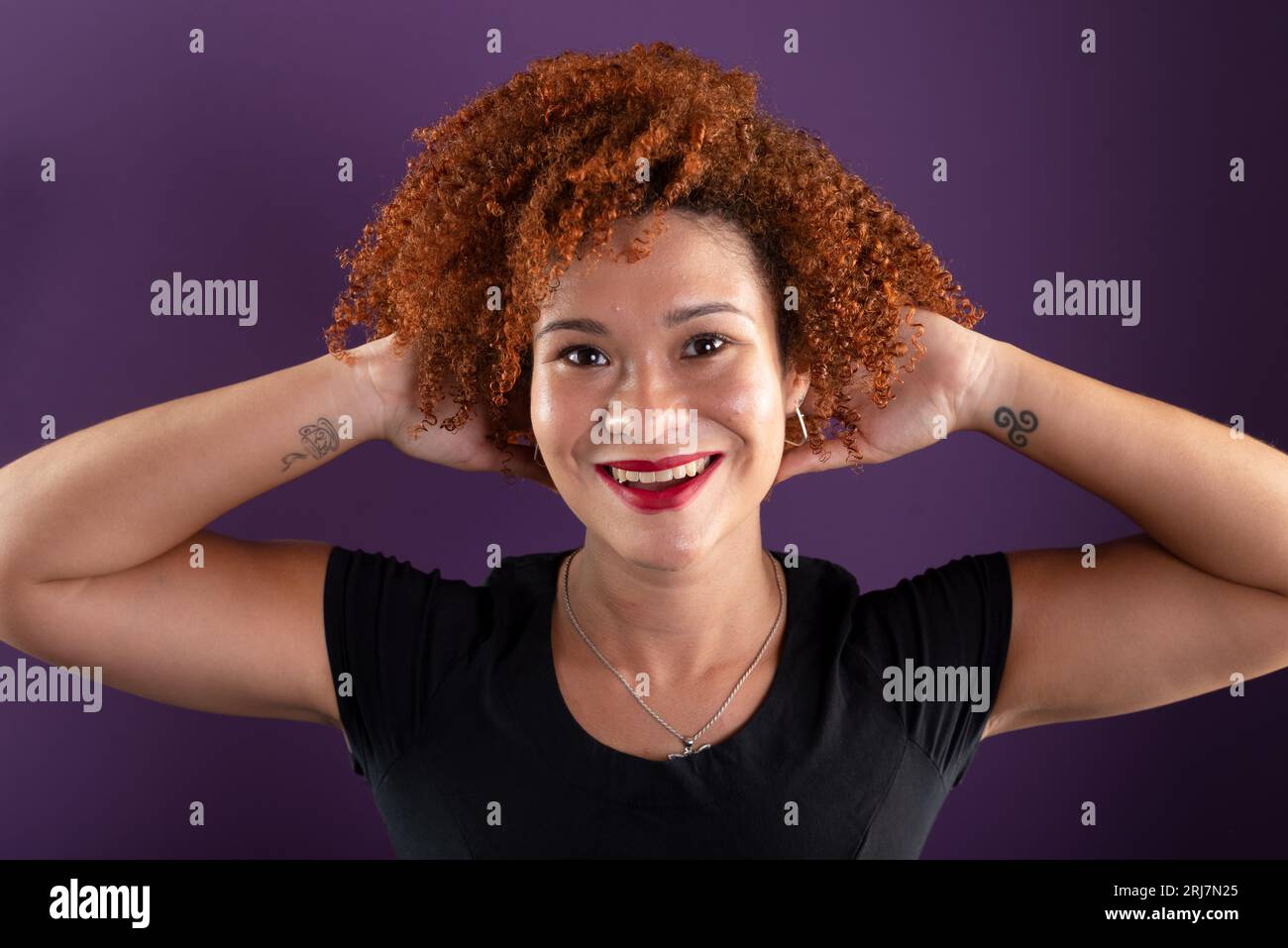 an attractive red-haired woman posing for a photo in black clothing touching her hair. Confident and happy. Isolated on lilac colored background. Stock Photo