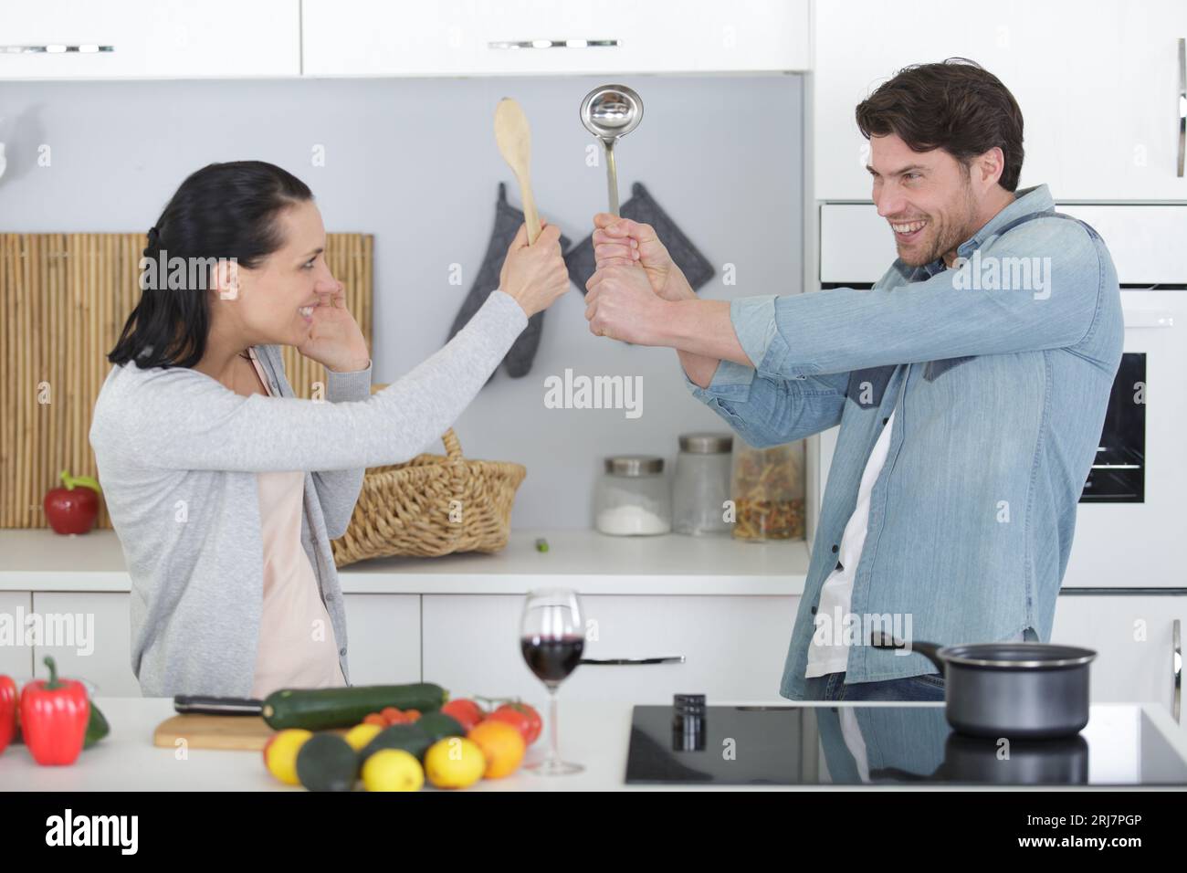 funny couple pretending fight with utensils tools while cooking Stock Photo