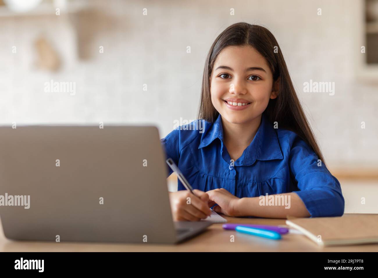 Teenage school girl posing at desk with laptop writing indoors Stock Photo