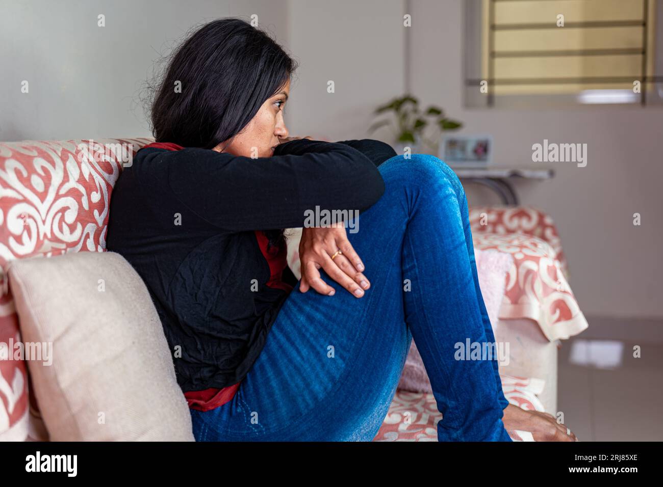 A close-up of a sad woman sitting on a sofa, her head in her hands. She ...