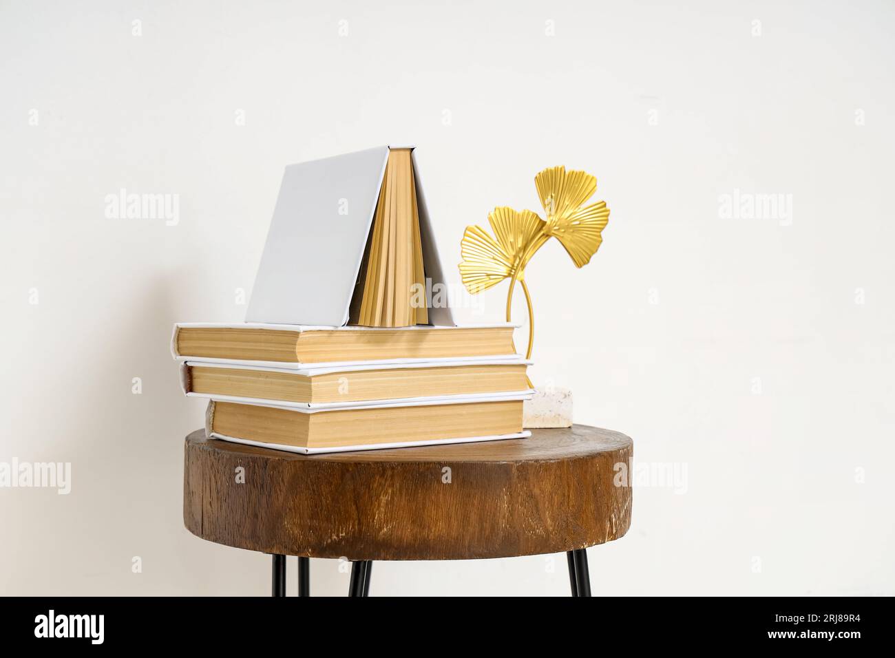 Stack of books with decor on table near light wall Stock Photo