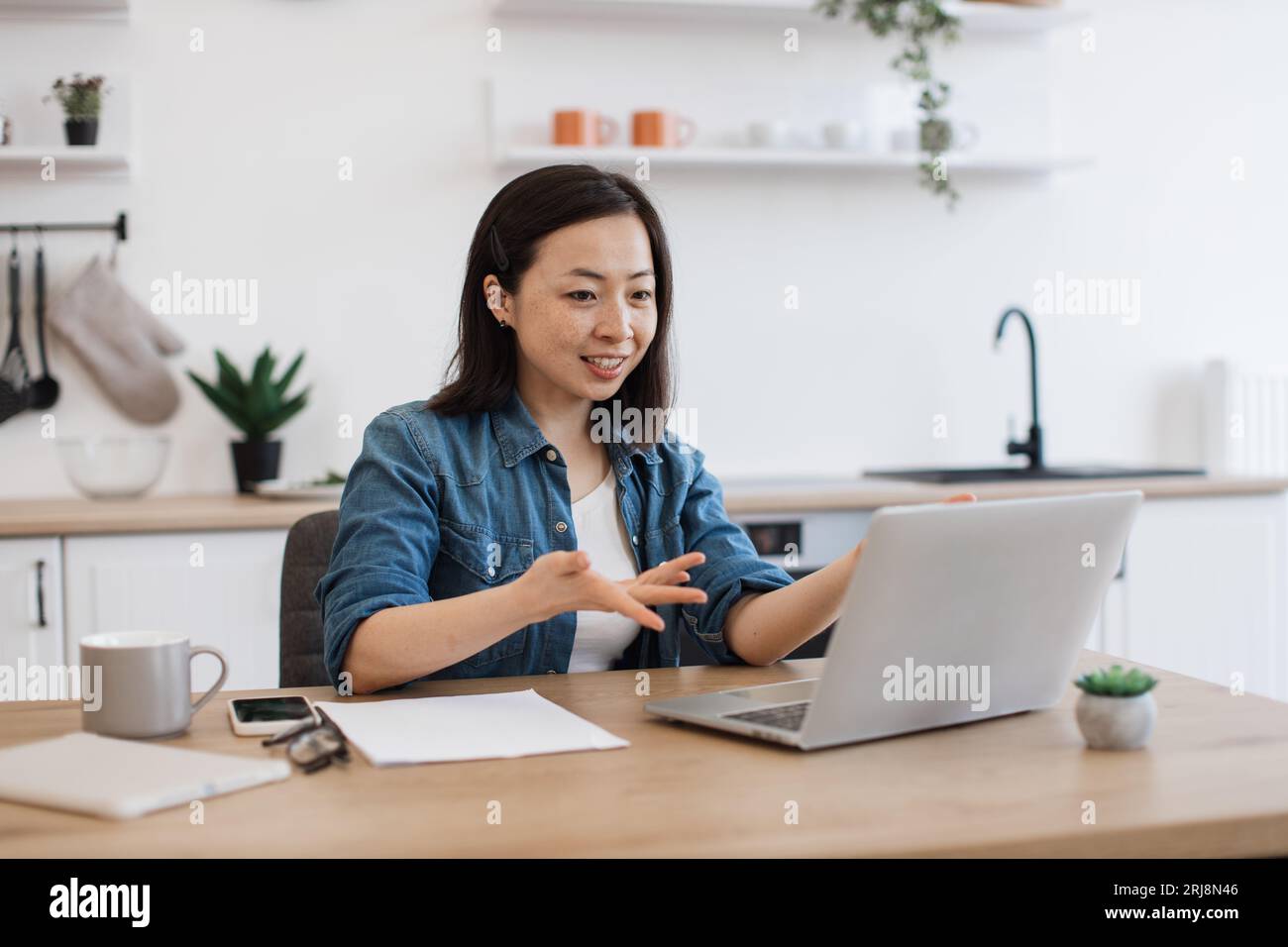 Smiling asian lady starting video call via internet app on laptop