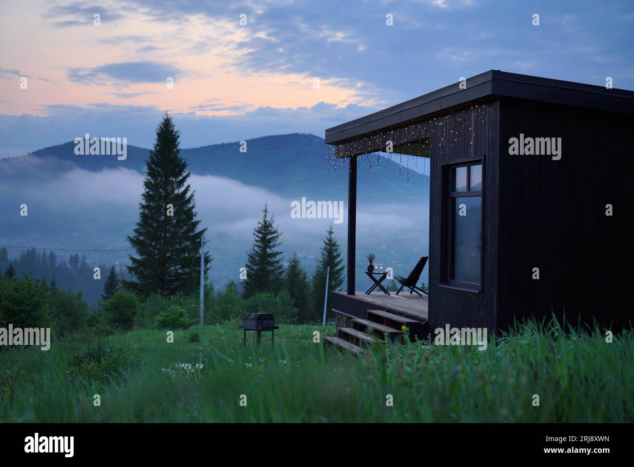 black wooden cabin with foggy mountain view evening at blue hour Stock Photo