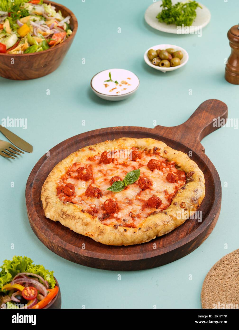 A close-up image of a freshly made pizza on a wooden board alongside other assorted dishes Stock Photo
