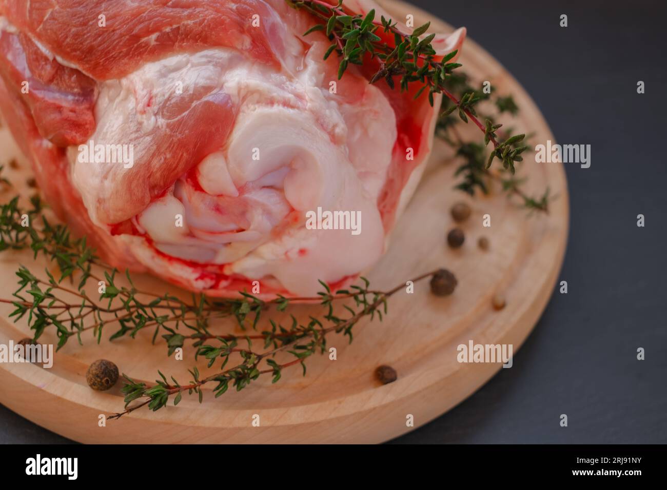 Pork knuckle. Pork meat on the bone, peppercorns, fresh thyme on a black slate background. Stock Photo