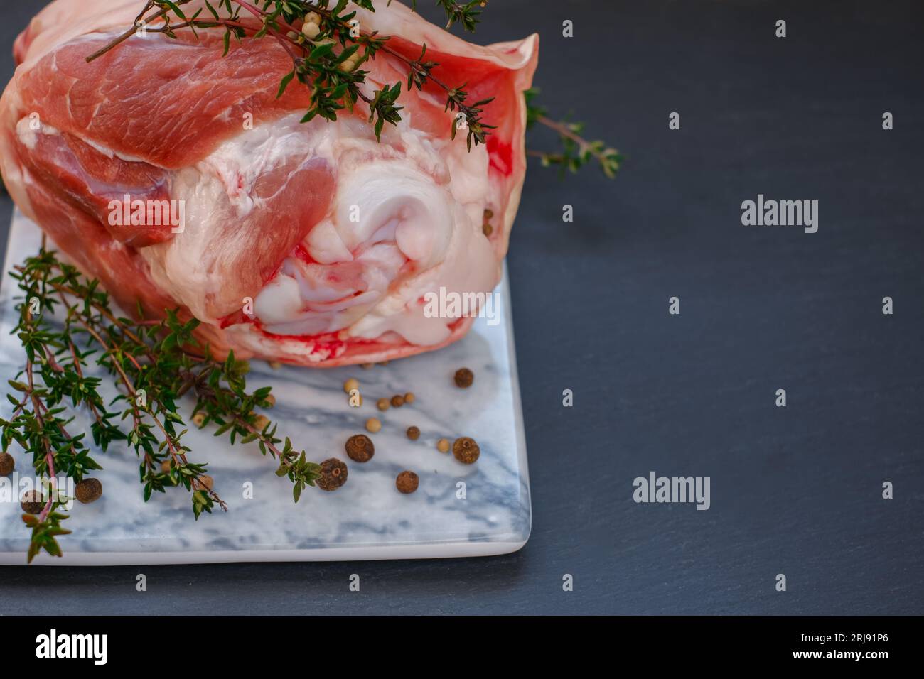 Pork knuckle.Pork meat on the bone.Pork knuckle, peppercorns, fresh thyme on a marble board Stock Photo