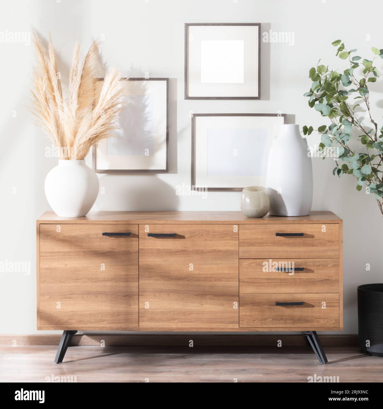 A wooden sideboard featuring three ceramic pots and frames hanging on