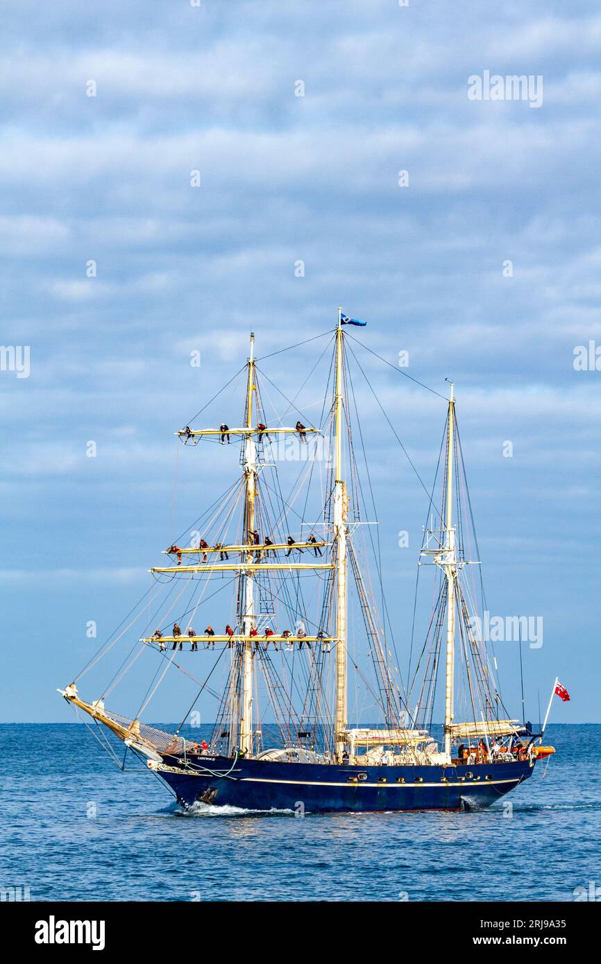 STSLeeuwin II,  a three-masted barquentine, returning to port with crew up rigging on yards. Stock Photo