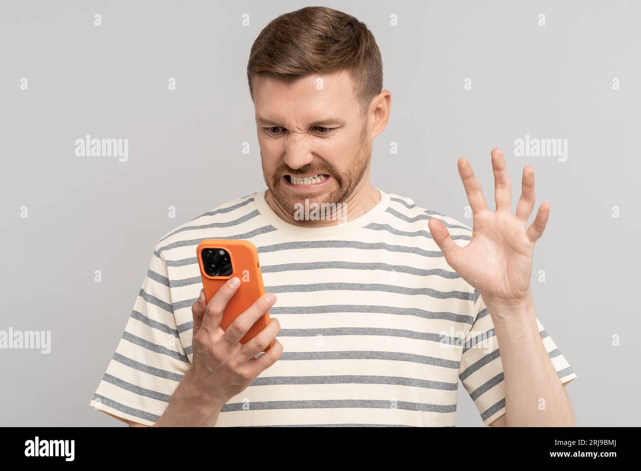 Unkind guy angry looks screen smartphone, aggressive video call, twisting face, making evil grimace. Stock Photo