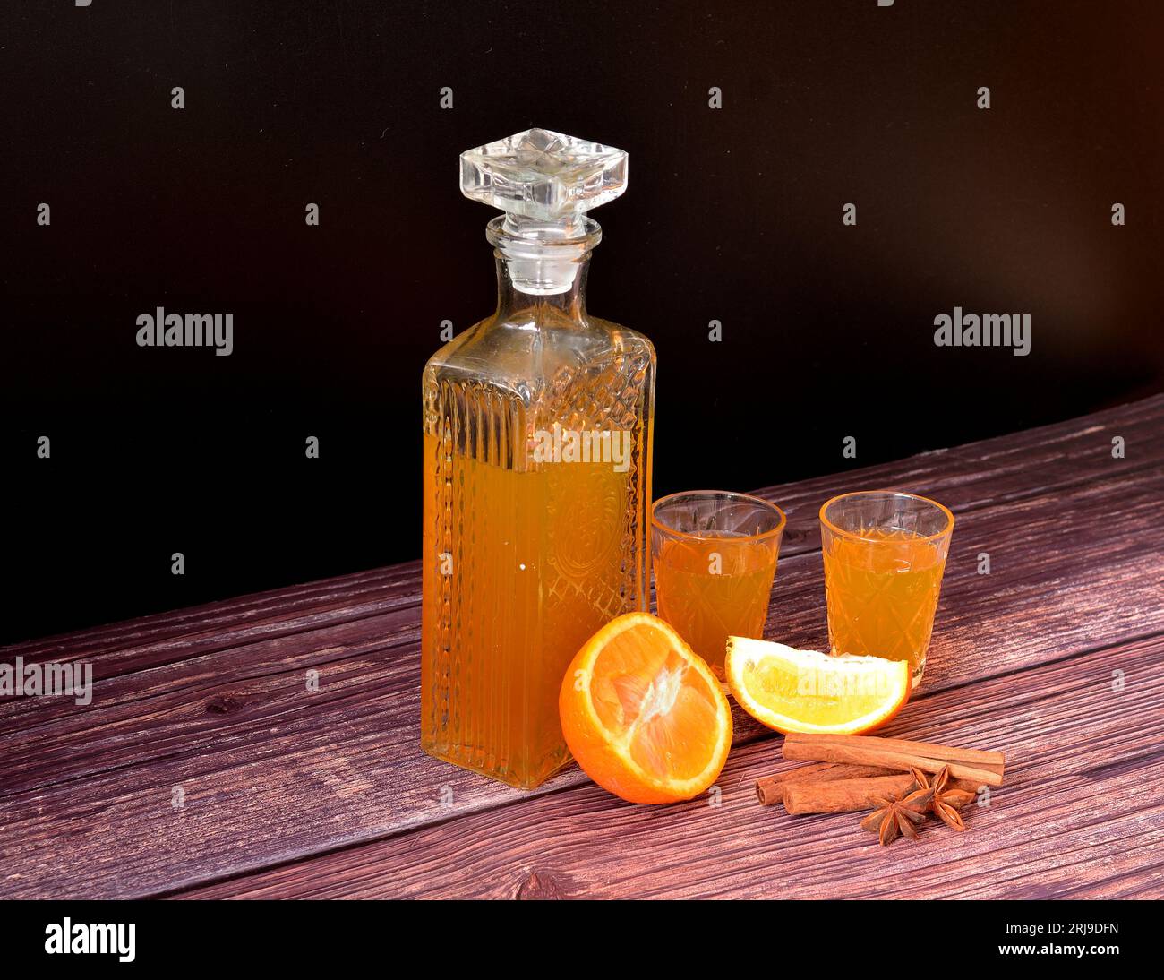 Orange liqueur on a dark wooden table, a bottle and two glasses with homemade alcohol, cinnamon and anise. Close-up. Stock Photo