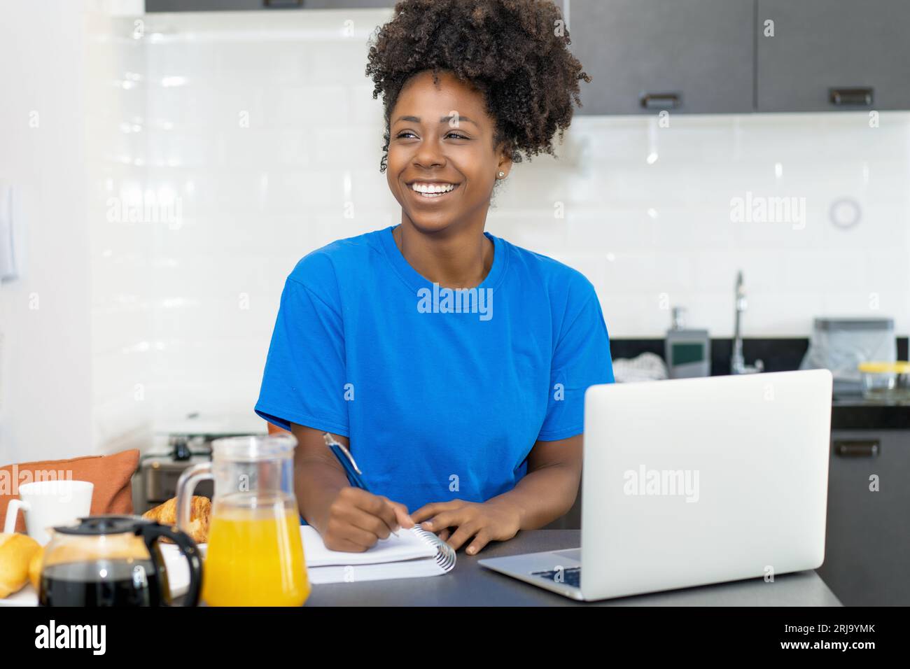 Laughing black woman with computer writing notes indoors at home at ...