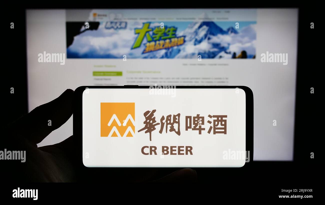 Person holding smartphone with logo of business China Resources Beer Holdings Co. Ltd. on screen in front of website. Focus on phone display. Stock Photo