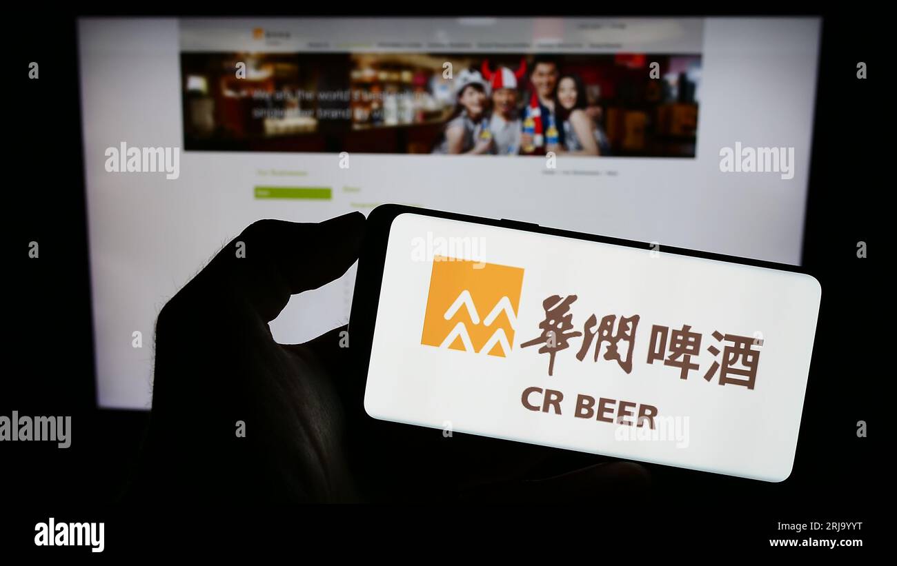 Person holding cellphone with logo of business China Resources Beer Holdings Co. Ltd. on screen in front of webpage. Focus on phone display. Stock Photo