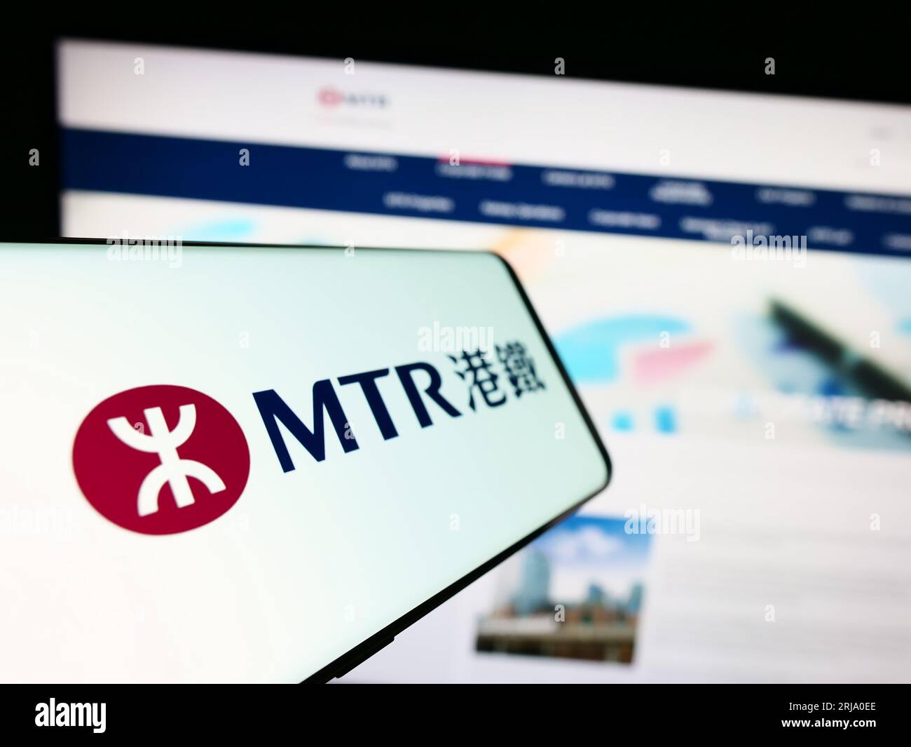 Mobile phone with logo of Chinese rail company MTR Corporation Limited on screen in front of website. Focus on center-left of phone display. Stock Photo