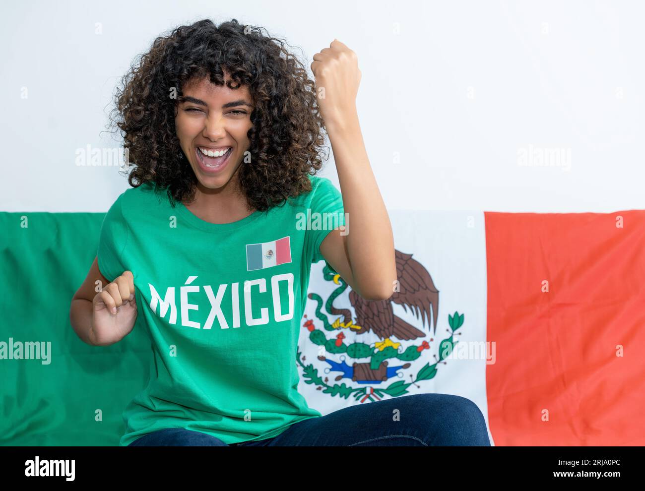 Cheering mexican female soccer fan with flag of Mexico indoors at home Stock Photo