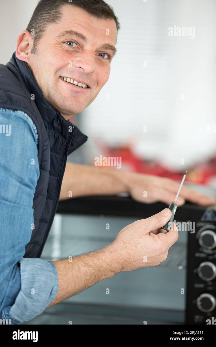 man with screwdriver repairing worktop oven Stock Photo