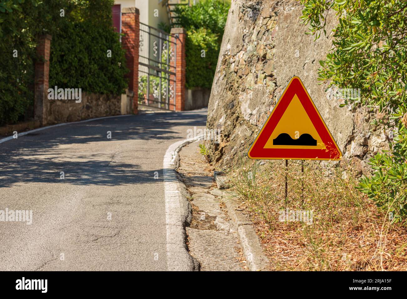 Triangular road sign of bumpy road. It is a danger sign that announces a deformed road, in bad condition, uneven or with irregular pavement. Stock Photo