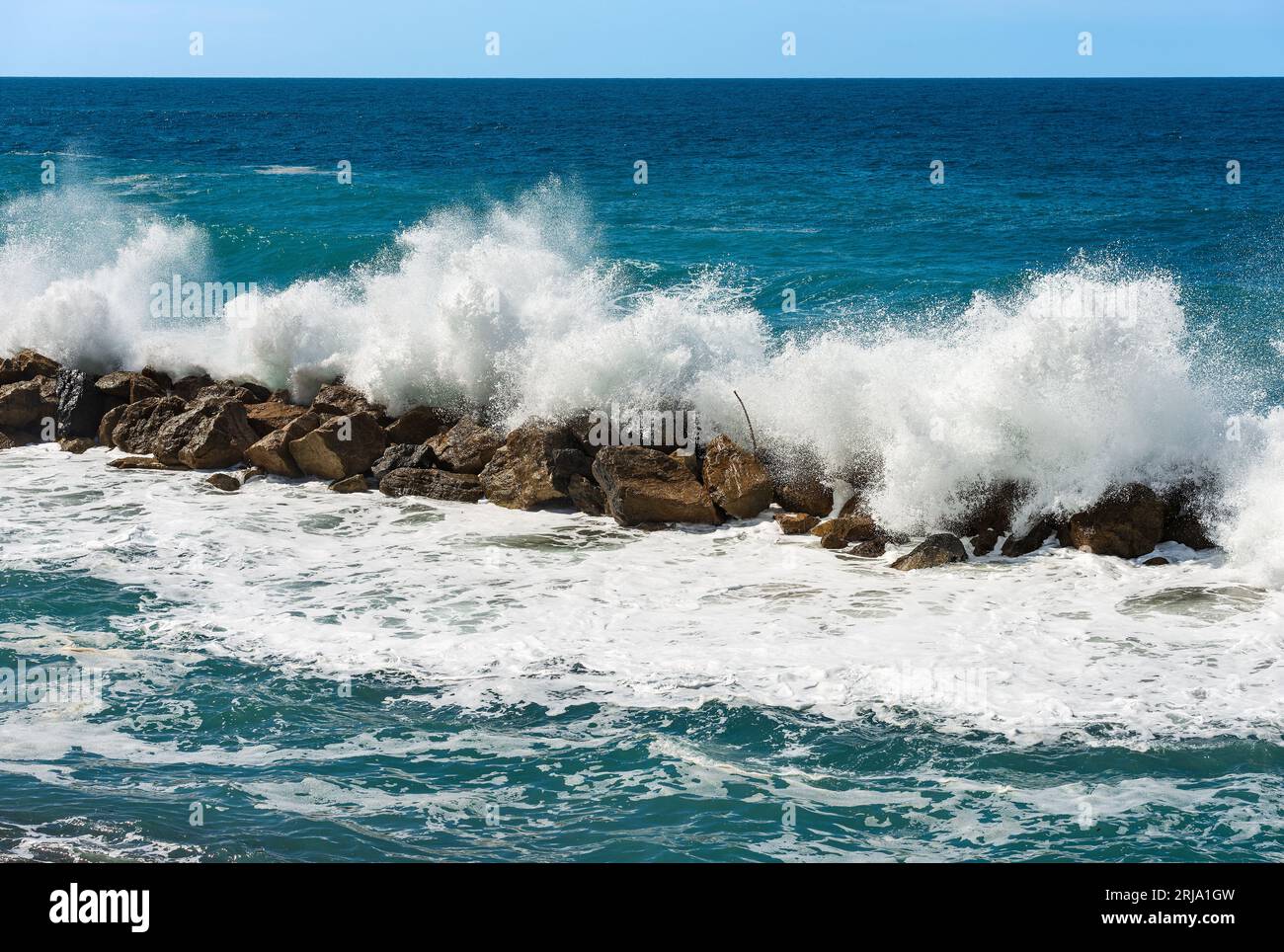 Large white waves of the sea break on the rocks. Breakwater near the small Village of Framura. La Spezia, Liguria, Italy, Europe. Mediterranean Sea. Stock Photo